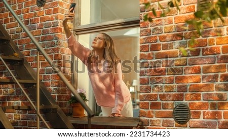 Annoyed Young Female Searching For Mobile Network Connection on Her Smartphone, Reaching Out with a Mobile Phone from an Apartment Window in Urban Neighbourhood.