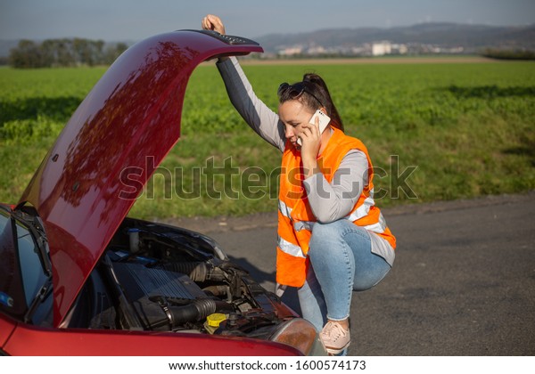 Annoyed young woman in a road distress situation\
- setting up a warning triangle and calling for assistance after\
her car broke down in the middle of nowhere; transportation concept\
(car problem)