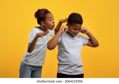 Annoying Older Sister African American Girl Scolding Little Brother, Irritated Black Boy Covering Ears While His Sibling Telling Him Something, Yellow Background. Brotherhood, Sisterhood Concept