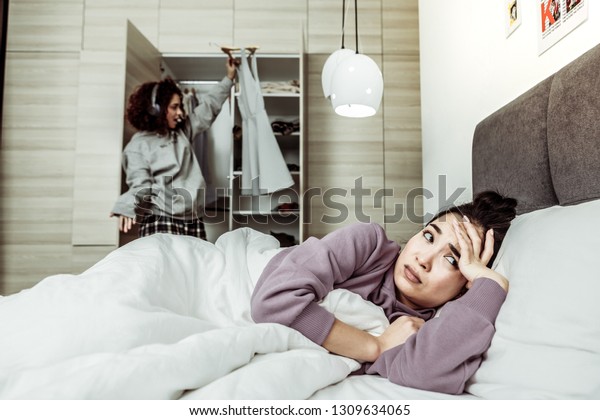 Annoying roommate. Dark-eyed woman\
lying in bed feeling tired of her annoying\
roommate