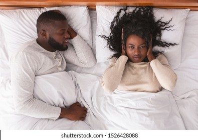 Annoying Snoring. Young Black Woman Closing Ears With Hands Suffering From Loud Snore Of Her Sleeping Husband.