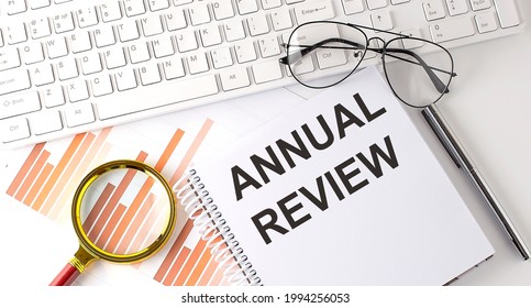 ANNUAL REVIEW text written on notebook with keyboard, chart,and glasses - Shutterstock ID 1994256053