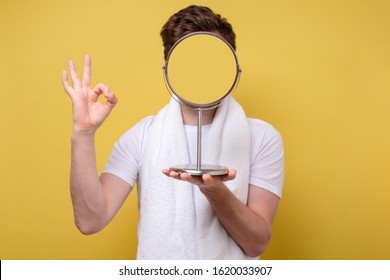 Anonym man looking at himself in the bathroom mirror shwoing ok sign. Noface view. Yellow wall. Studio shot