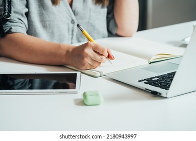 An Anonymous Businesswoman Writing Business Report While Sitting At The Kitchen Desk With Laptop Computer, Digital Tablet And Wireless Earphones