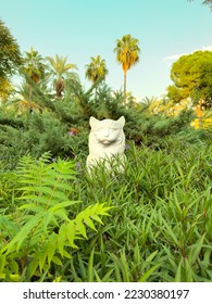 anonymous cat sculpture and trees rising through flowers, cat statue looking through the flowers, sculpture in park