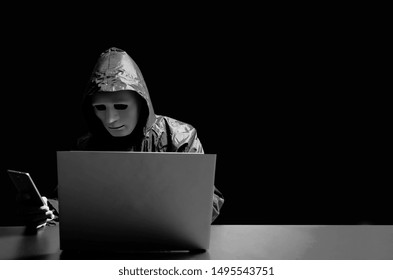 Anonymous computer hacker in white mask and hoodie. Obscured dark face attacking people through a smartphone. contacting victom by texting and asking for more money, Data thief, internet attack. - Powered by Shutterstock