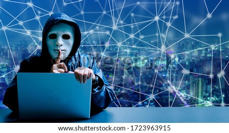 Anonymous computer hacker in white mask and hoodie. Obscured dark face making silence gesture on modern city background, Data thief, internet attack, darknet and cyber security concept.