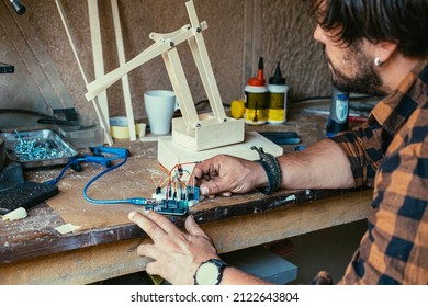 An Anonymous Engineer Working On A Robot Arm. 
Close Up Photo Of Man Hands Holding Wires And Making Robotic Arm In His Workshop.