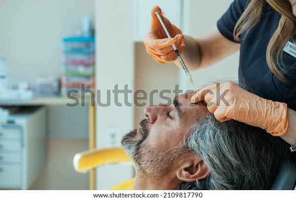 An\
Anonymous Female Beautician Giving Male Patient Botox Injection In\
Forehead. \
\
Anti Aging Treatment: Side view of mature man\
receiving botulinum toxin injection at medical\
clinic.