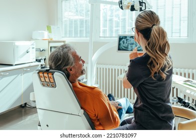 An Anonymous Female Dentist Explaining Teeth X-ray on a Digital Tablet to Smiling Mature Patient at Dentist's Office - Powered by Shutterstock