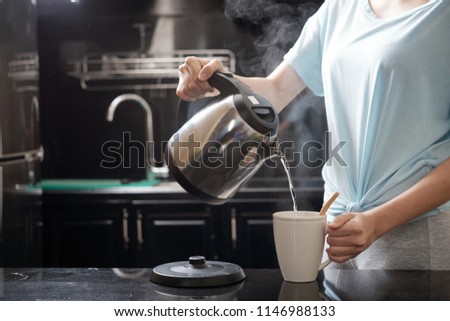 Anonymous female filling mug with hot water while brewing beverage in kitchen
