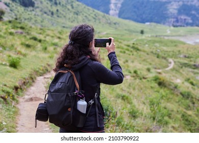 Anonymous female hiker with curly hair photographing a beautiful landscape with her smartphone