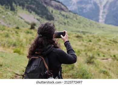 Anonymous female hiker with curly hair photographing a beautiful landscape with her smartphone