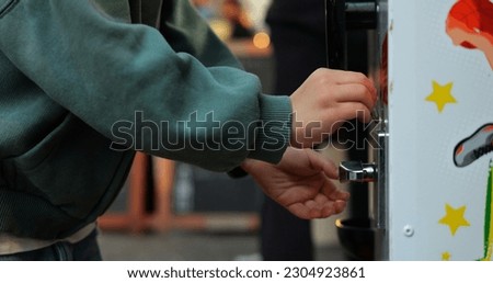 Anonymous five year old child insert coin into gashapon or gumball machine. Closeup shot of preschool kid make payment to buy bubble gum ball from vending machine. High quality photo