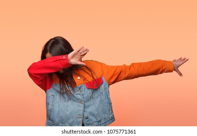 Anonymous girl in colorful denim jacket standing in dab dance pose on orange background. 