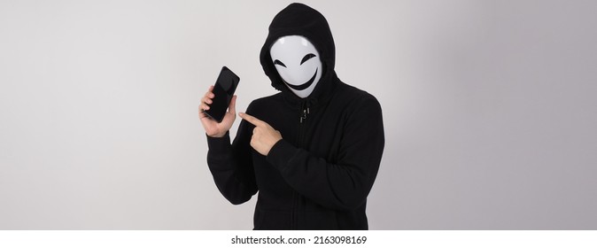 Anonymous hacker and face mask with smartphone in hand. Man in black hood shirt holding and using mobile phone on white background. Represent cyber crime data hacking or stealing personal data concept