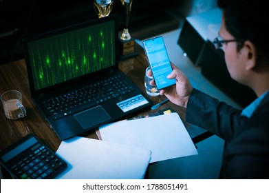 Anonymous hacker programmer uses a laptop and mobile phone to hack the system in the dark. Concept of cyber crime and hacking database.