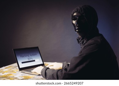 Anonymous hacker programmer uses a laptop to hack the system in the dark. The concept of cybercrime and hacking database. Money is scattered on the table. Focus on laptop