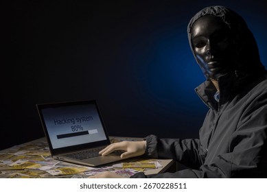 Anonymous hacker programmer uses a laptop to hack the system in the dark. The concept of cybercrime and hacking database. Money is scattered on the table. Focus on laptop