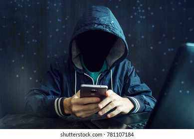 An anonymous hacker without a face uses a mobile phone to hack the system. Stealing personal data and money from Bank accounts. The concept of cyber crime and hacking electronic devices
