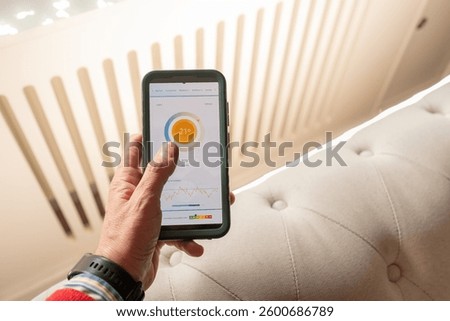 An anonymous hand controls the temperature of an intelligent home equipped with Wireless home automation technology using an app on your mobile phone. A heating radiator on the bottom