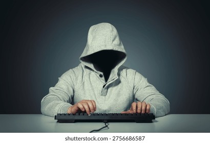 Anonymous hooded hacker sitting at computer and typing on keyboard in a dark room. Faceless silhouette creates a mysterious cybercrime atmosphere. Concept of cybersecurity threat, data breach, online attack, identity protection, digital espionage, network intrusion, and underground hacking activity. Dramatic low key lighting emphasizes secrecy and danger in the modern technology world.