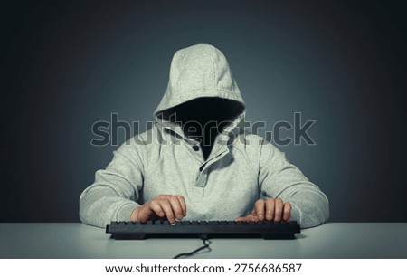 Anonymous hooded hacker sitting at computer and typing on keyboard in a dark room. Faceless silhouette creates a mysterious cybercrime atmosphere. Concept of cybersecurity threat, data breach, online attack, identity protection, digital espionage, network intrusion, and underground hacking activity. Dramatic low key lighting emphasizes secrecy and danger in the modern technology world.