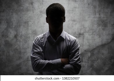 Hombre anónimo en un pantalones de negocios con los brazos cruzados en un fondo oscuro