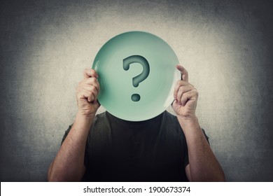Anonymous man hiding his identity, covering face using an empty dish plate with question mark. Global crisis, food supply problem. Conceptual message, starvation and famine issue. Hunger diet concept