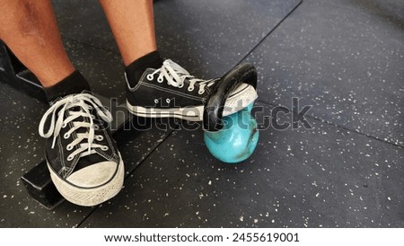 An anonymous man performs a variation of standing one leg Anterior Tibialis Raises with a kettlebell at the gym.