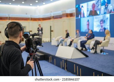 Anonymous Man Recording Video Of Businesspeople Talking From Stage And Large Monitor During Business Conference In Light Auditorium