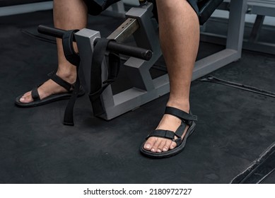 An anonymous man wearing sandals while using the incline bench press. Improper or casual footwear for working out at the gym.