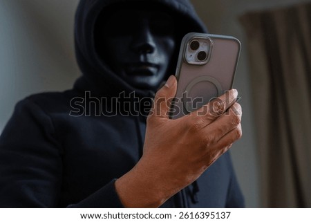 An anonymous masked hacker is using a smartphone to penetrate credit card financial information. Hacking and malware concept.