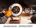 Anonymous mechanic in jacket and gloves while standing in workplace in automobile garage and replacing car wheel brake pad against blurred interior in daylight