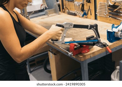 anonymous mechanical girl cutting a pipe attached to a vise with a saw in a workshop - Powered by Shutterstock