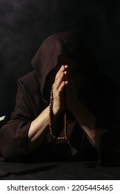 Anonymous Monk In Hooded Robe Praying With Rosary Beads Isolated On Black