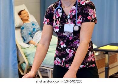 An Anonymous Nursing Student In Scrubs With A Stethoscope Learning In A Simulation Lab With A Mannequin Patient In The Background 