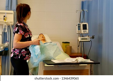 An Anonymous Nursing Student In Scrubs With A Stethoscope Learning In A Simulation Lab With A Mannequin Patient In The Background 