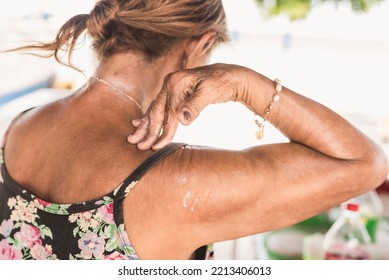 An Anonymous Old Woman Reaches Her Back Applying Sunscreen Lotion. Using Sunblock Outside, Possibly At The Beach.