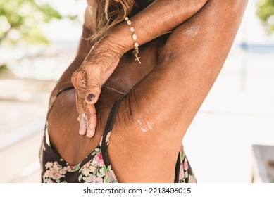 An Anonymous Old Woman Reaches Her Back Applying Sunscreen Lotion. Using Sunblock Outside, Possibly At The Beach.