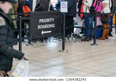 Anonymous passengers in queue behind PRIORITY BOARDING sign at the airport. All brands/logos removed