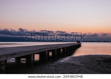 Anonymous persons sitting on pier near sea at sunset
