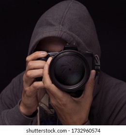 Anonymous Photographer In A Hoodie Shooting With Camera On Black Background