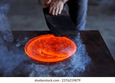 Anonymous professional male master working with hot orange glass carefully at dark table with smoke in factory - Powered by Shutterstock