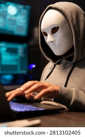 Anonymous programmer conceals identity while typing malicious code on laptop, hacker works late at night and targets company networks, online crime and data breaches.