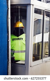 An anonymous security man standing inside a booth, guarding a construction site.
