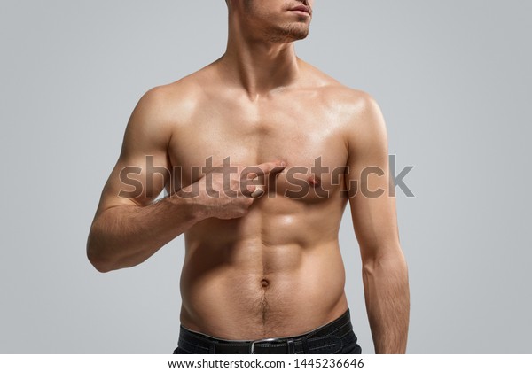 Anonymous shirtless athlete pointing at\
pectoral muscle after workout against gray\
background
