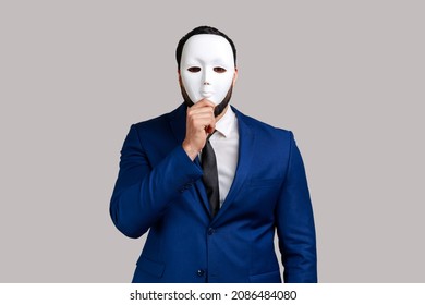 Anonymous unknown businessman covering her face with white mask, hiding her real personality, anonymity, wearing official style suit. Indoor studio shot isolated on gray background.