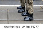 Anonymous unrecognizable generic infantry army soldiers standing at attention in a row on the street, legs boots closeup detail shot, copy space, green camo uniforms. Military operations border patrol