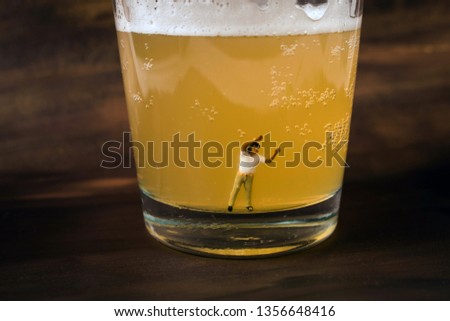 Anonymous, unrecognizable miniature man in a glass of beer. Binge drinking concept. Tiny person with a drinking problem at a crazy party. Last call, or time to seek help with a drinking problem. 